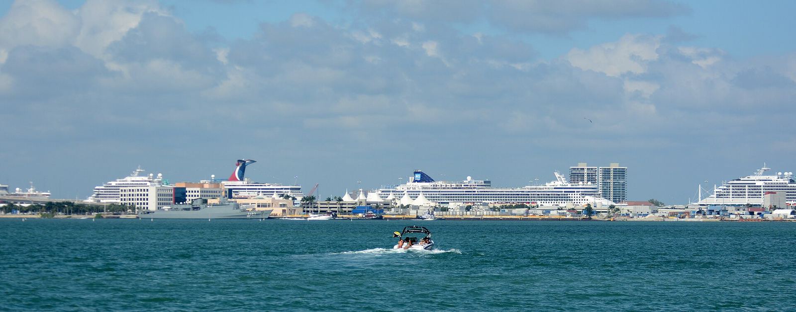 Cruise ships docked at the port in Miami, seen across the water with a small boat in the foreground
