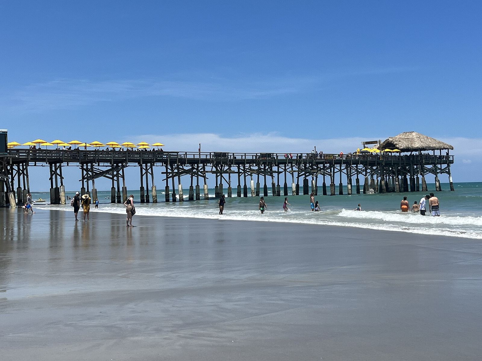 Cocoa Beach pier stretching into the ocean, with people wading in the shallow surf