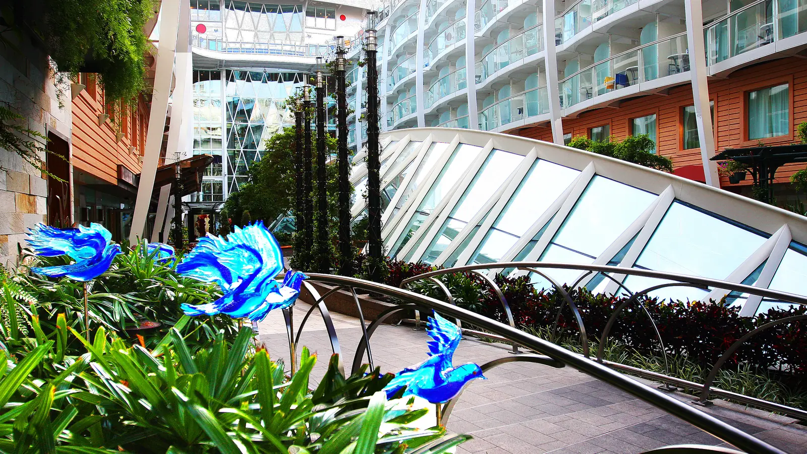 Tropical plants, glass bird sculptures and balconies in an open-air park area on a big family cruise ship