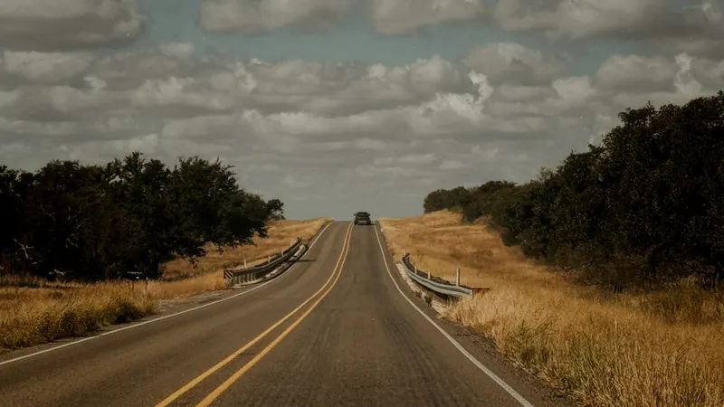 Long, empty two-lane road under a cloudy sky