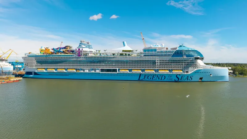 Very large new cruise ship with waterslides on top, moored at a shipyard under blue sky