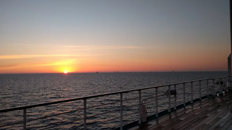 Sun setting over a calm sea seen from a cruise ship deck rail