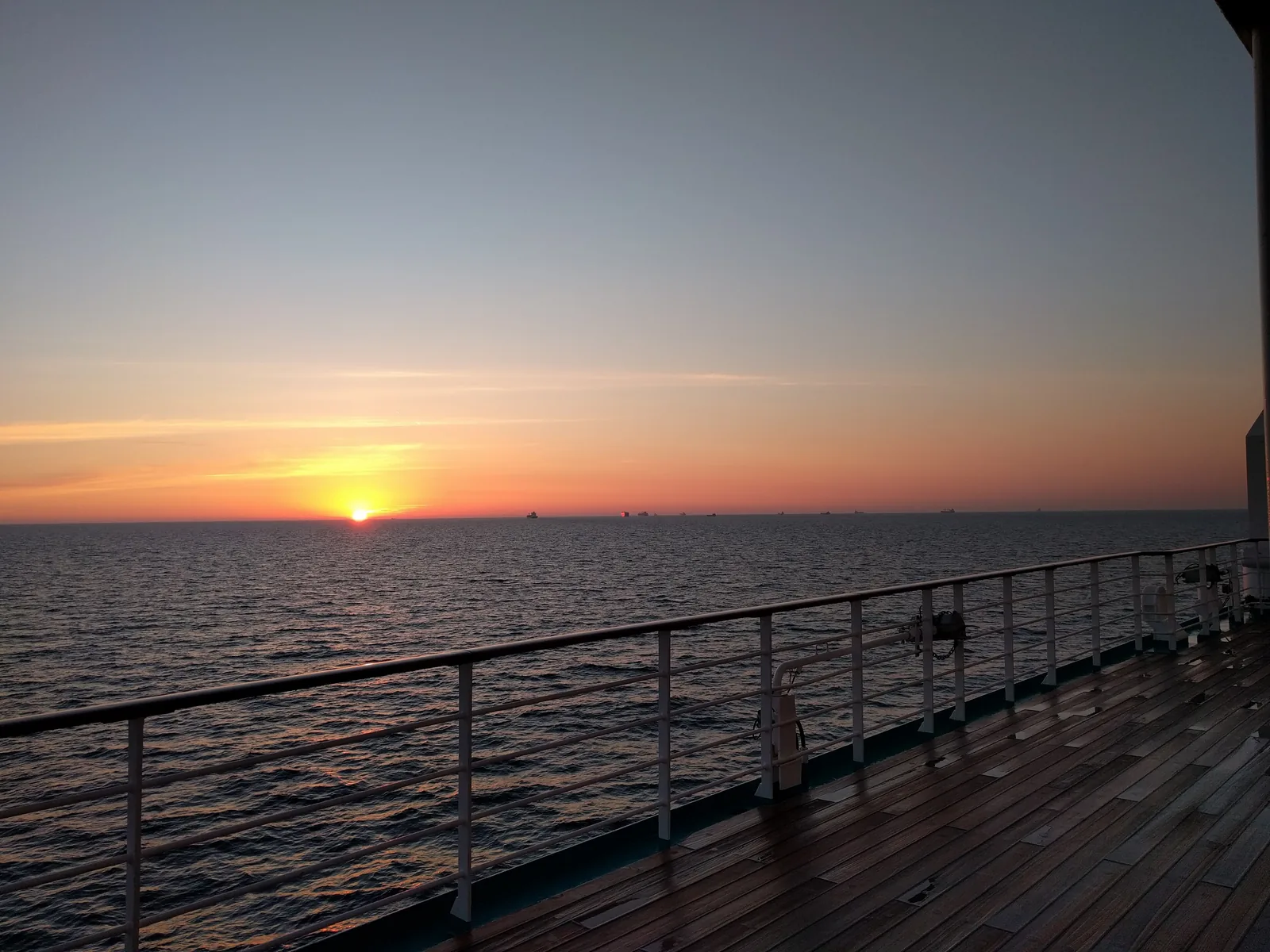 Sun setting over a calm sea seen from a cruise ship deck rail