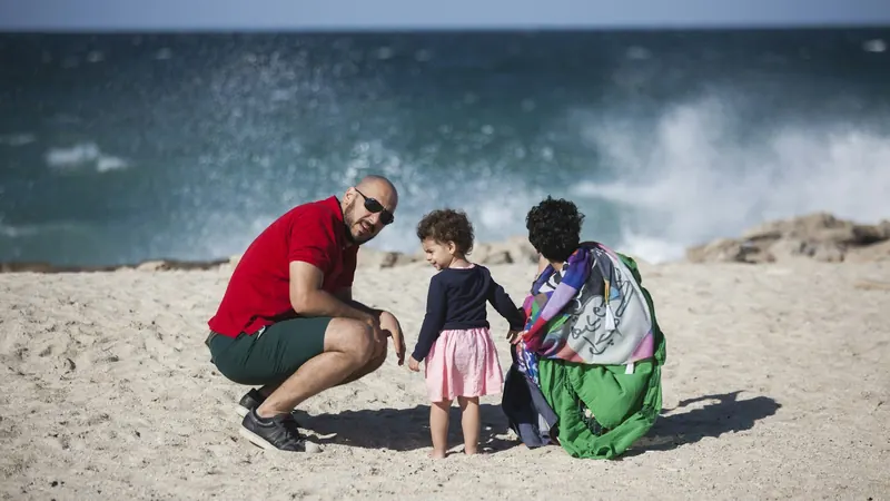 Man and woman crouching with a little girl on a windy beach