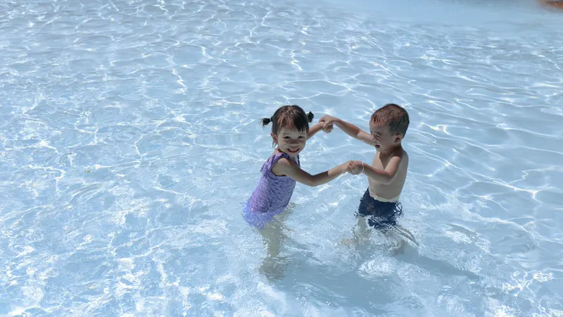 Two young children splashing together in a shallow pool