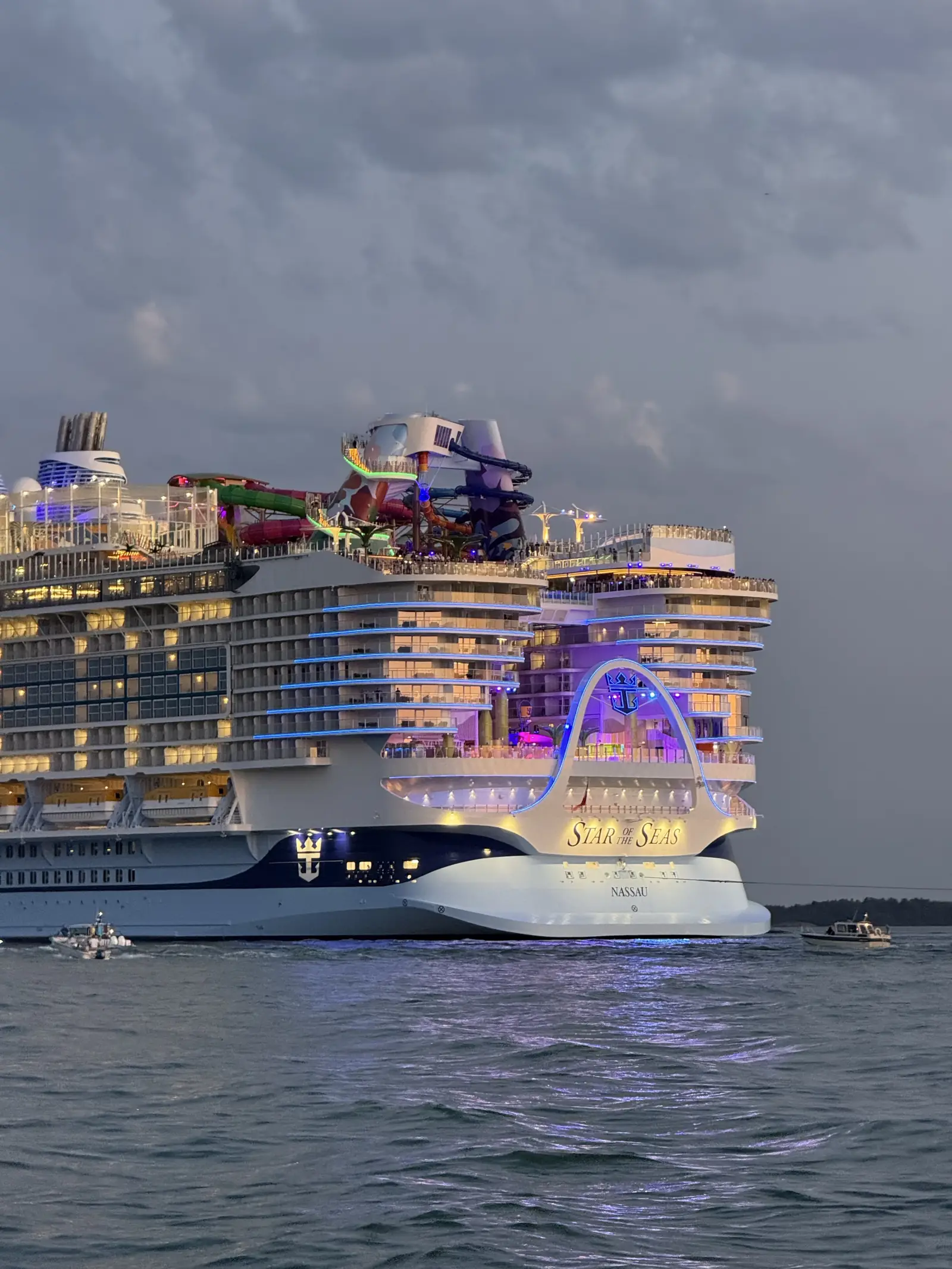 Very large cruise ship lit up at dusk on gray water