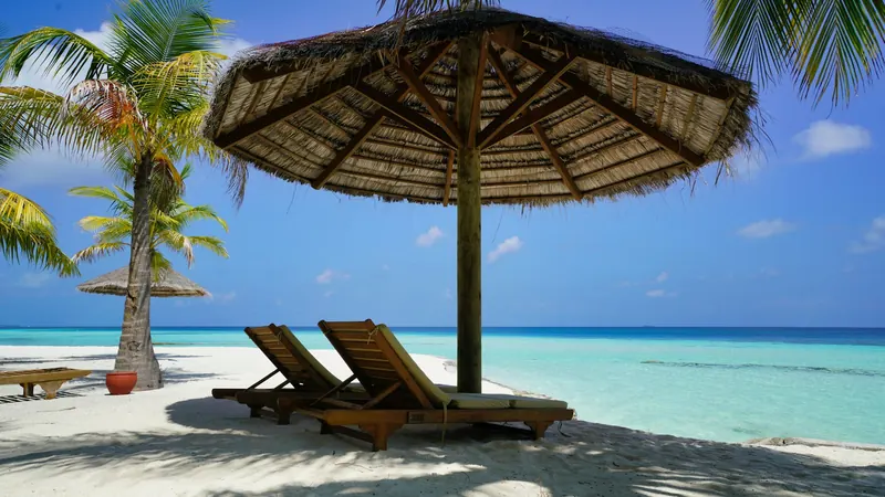 Thatched beach umbrella shading two loungers on white sand by turquoise water