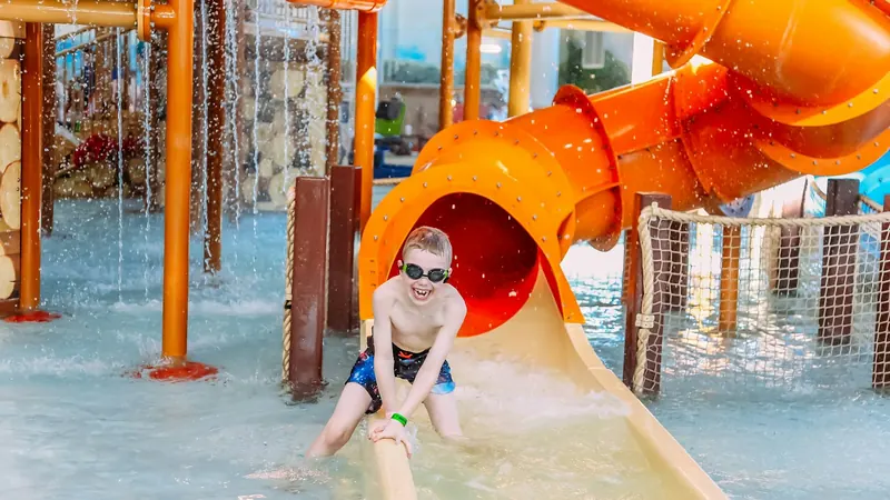 Smiling boy in goggles sliding down a water slide into a splash pool