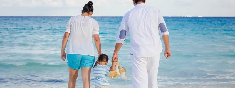 Family walking hand in hand along a sunny beach, seen from behind