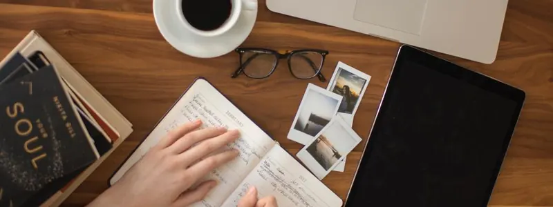 Hands writing in a notebook beside a laptop and coffee while planning a vacation
