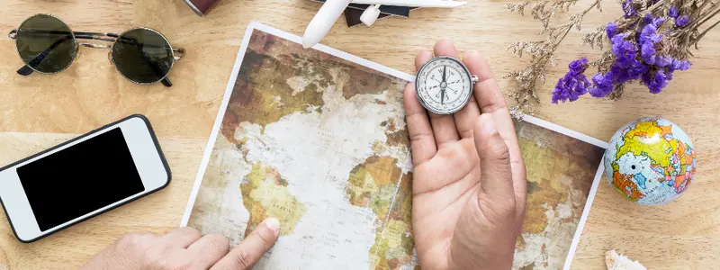 Travel planning flat-lay with a map, compass, camera and phone on a wooden table