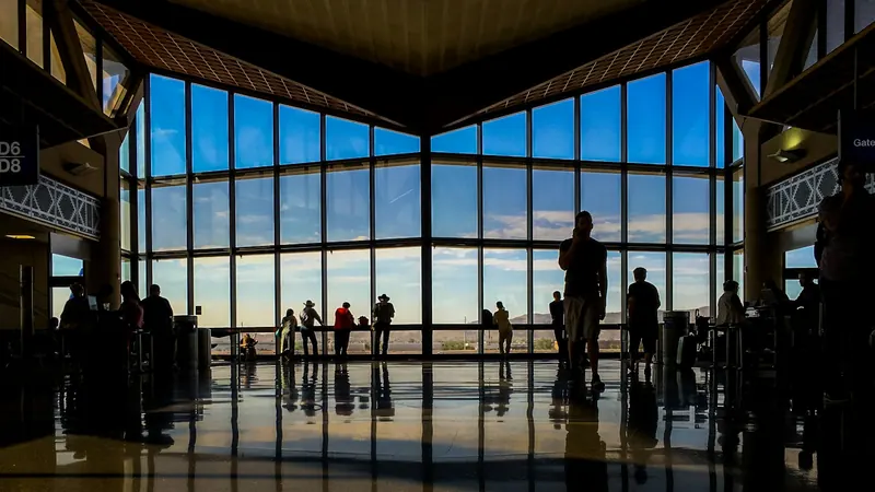 Travelers silhouetted against tall windows in an airport terminal
