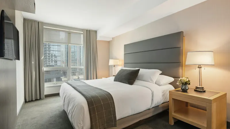 Bright hotel room with a made bed, bedside lamps and a large window