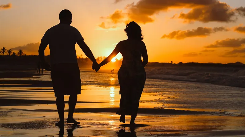 Couple holding hands as they walk along the beach at sunset