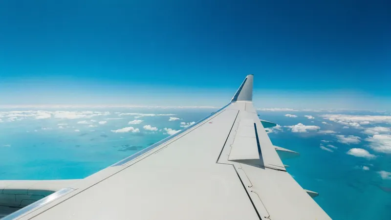 View from an airplane window of the wing over turquoise water and clouds